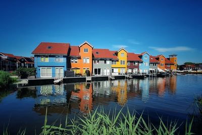 Buildings by lake against blue sky