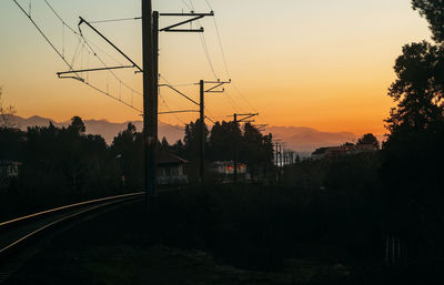 Silhouette trees by electricity pylon against sky during sunset