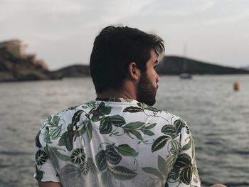 Rear view of man looking away while standing against sea