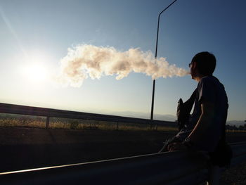 Side view of man standing by railing against sky during sunset