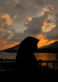 Silhouette woman looking at lake against sky during sunset