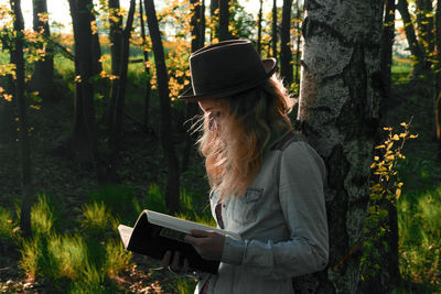 Woman reading book by tree trunk in forest