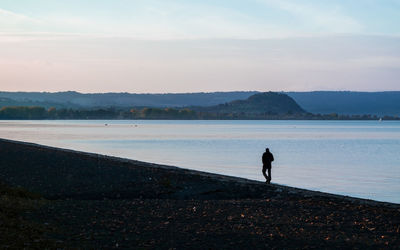 Silhouette man standing on lake against sky