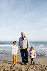 Portrait of happy grandfather standing hand in hand on the beach with his grandchildren