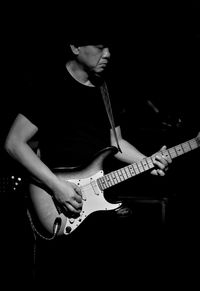 Midsection of man playing guitar against black background
