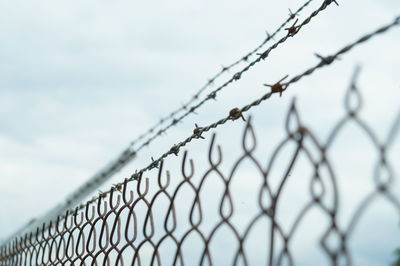 Close-up of barbed wire fence against sky