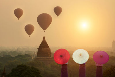 People with umbrellas standing against temple during sunset