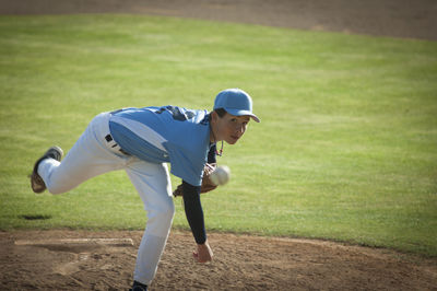 Pitcher in light blue and white jersey during wind up on a baseball field.