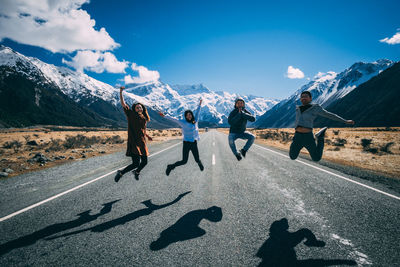 4 friends jump higher on the road with snow capped mountains at the back. new zealznd. road trip