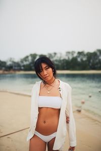 Portrait of young woman standing at beach against sky