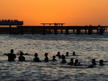 Silhouette people by sea against sky during sunset