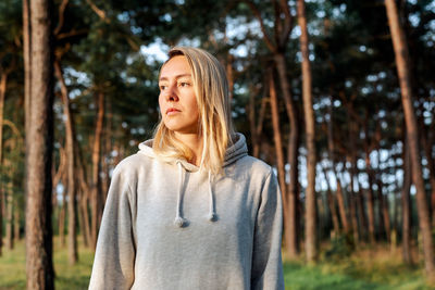 Portrait of a young blond woman walking in a pine forest at dawn.