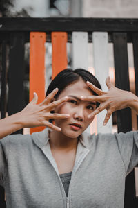 Young woman gesturing over face while looking away against railing