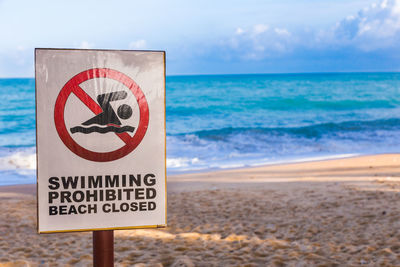 Warning sign on beach against sky