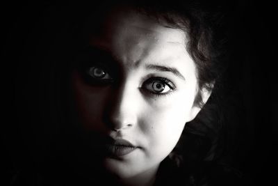 Close-up portrait of young woman against black background