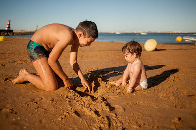 Full length of shirtless boys on beach against sky