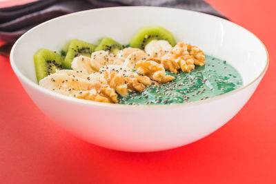 A spirulina smoothie bowl with banana, walnuts, kiwi and chia seeds on red background