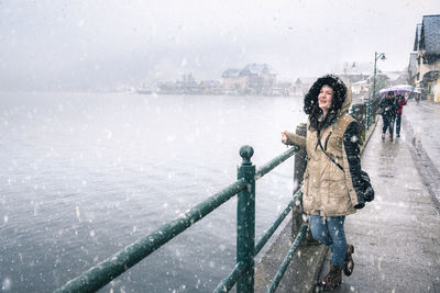 Young woman wearing fur coat while standing on road during snowfall in city