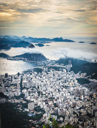 Aerial view of townscape by sea against cloudy sky during sunset