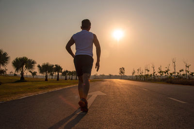 Rear view of man running on road against sky during sunset