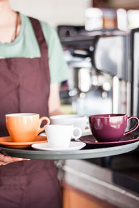 Midsection of waitress holding coffee cups in tray at restaurant