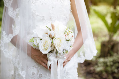 Midsection of woman holding bouquet against white wall