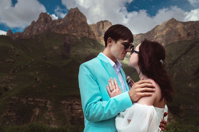Beautiful wedding couple laughs and plans to kiss against the backdrop of mountains and cloudy sky
