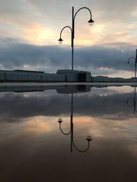 Silhouette street light by pond against sky during sunset