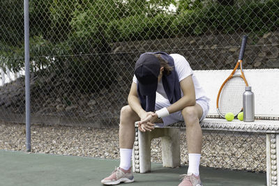 Exhausted sportsman sitting on a bench after tennis training class looking down to the floor 