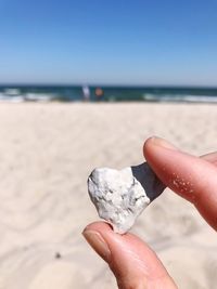Close-up of hand holding sand at beach against sky