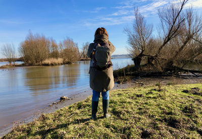 Rear view of a woman that looks out over flooded land with bare trees under blue sky