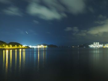 Illuminated city by sea against sky at night