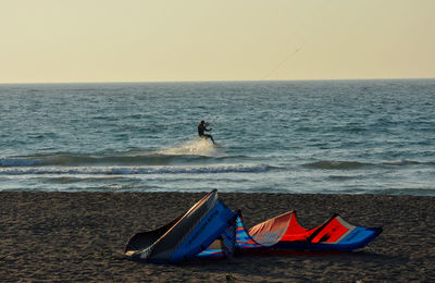 Kite at beach by silhouette man surfing in sea against clear sky