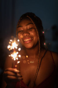 Portrait of young woman holding illuminated string lights at night