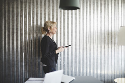 Side view of businesswoman talking on mobile phone against corrugated iron wall at creative office