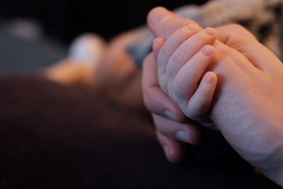 Cropped image of parent and baby holding hands on bed