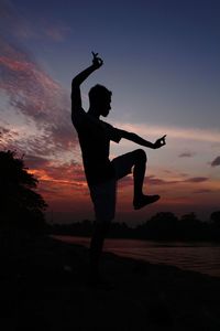Silhouette man with arms raised standing on land against sky during sunset