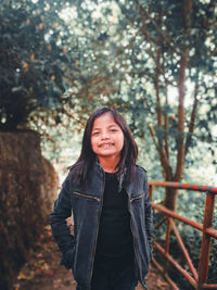 Portrait of smiling young woman standing against trees in winter