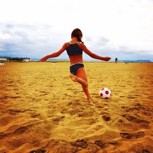 Rear view of girl kicking soccer ball at beach