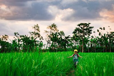 Boy walking on agricultural field against cloudy sky