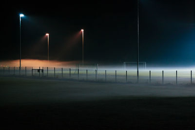 Illuminated street light on field against sky at night