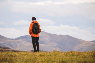 Rear view of man standing on field against mountains