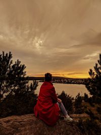 Rear view of woman sitting on rock against sky