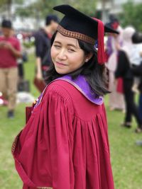 Side view of smiling woman wearing graduation gown while standing outdoors