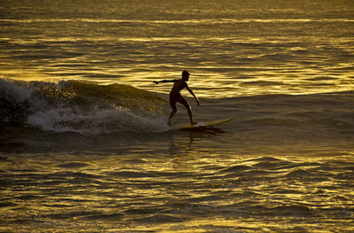 Silhouette man surfing in sea against sky during sunset
