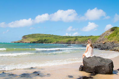 Woman sitting on beach looking at sea against sky