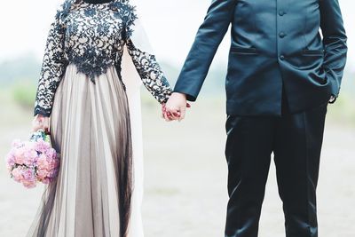 Midsection of bridegroom holding hands standing outdoors