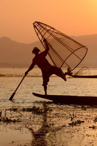 Fisherman fishing in lake with conical fishing nets during sunset