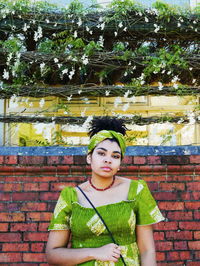 Portrait of young woman standing against brick wall