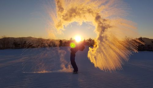 Man using distress flare on snow covered field against clear sky during sunrise